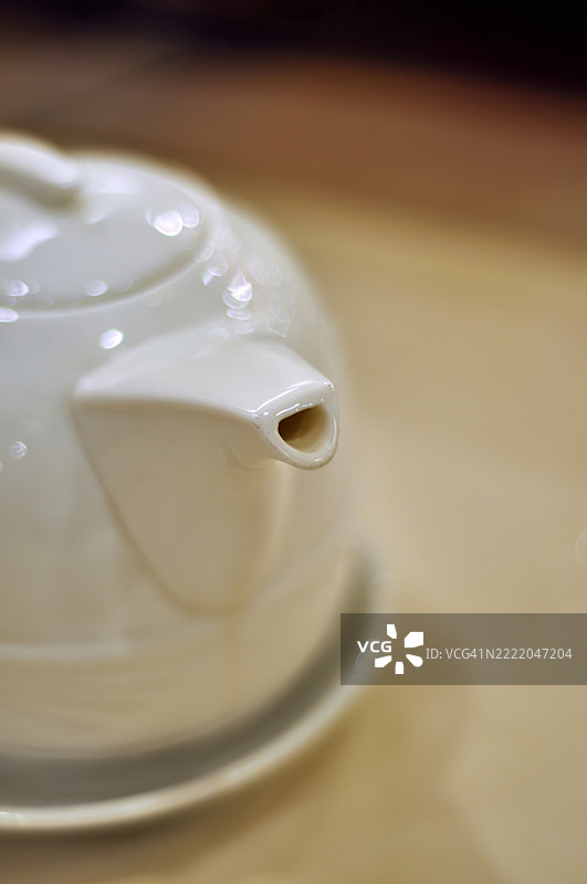 一只经典造型的白色瓷茶壶静静地放在浅色表面上。图片素材