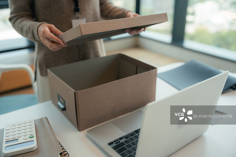 女性员工在安静地将个人物品打包进箱子，准备离开她的第一份工作。图片素材