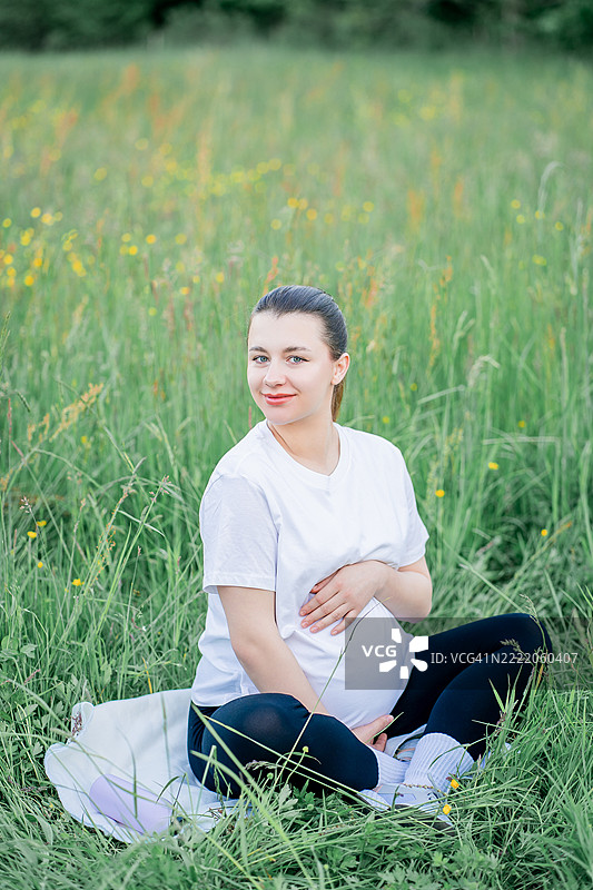 穿着运动服的年轻孕妇在城市外的街道上做瑜伽。公园里的康复运动。母亲身份。图片素材