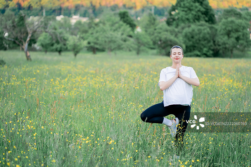 穿着运动服的年轻孕妇在城市外的街道上做瑜伽。公园里的康复运动。母亲身份。图片素材