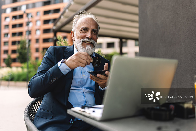 户外环境中，手拿咖啡的男子在笔记本电脑前工作图片素材