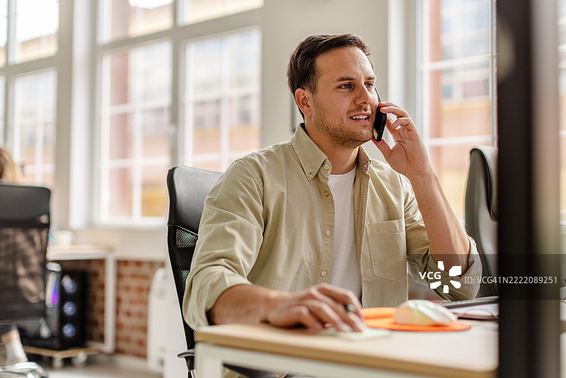 年轻人在现代办公室的桌子前打电话，白天工作。图片素材