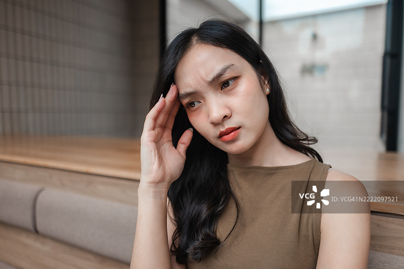 年轻的亚洲女性因头痛而感到不适，用手触摸额头，神情忧虑和担心图片素材