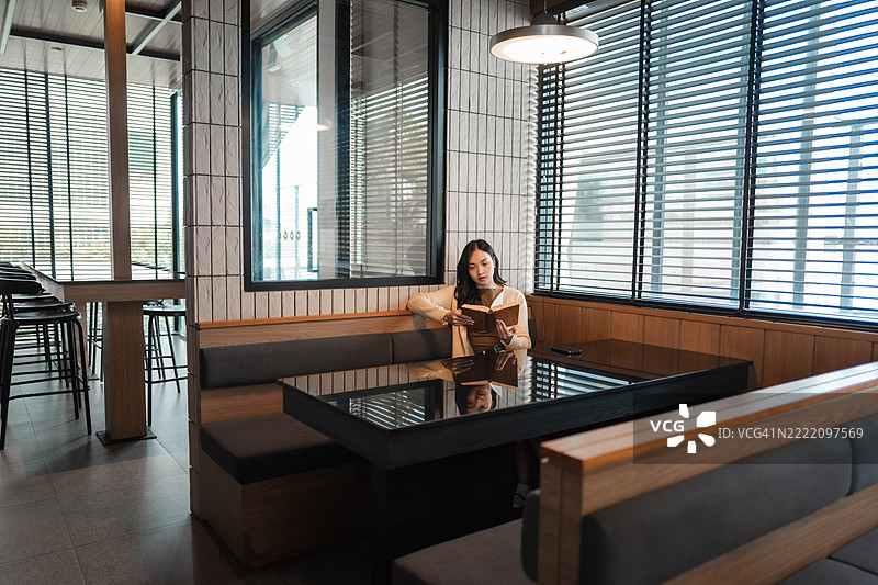 年轻女性在时尚咖啡馆中享受阅读，感受温馨氛围中的宁静与知识。图片素材