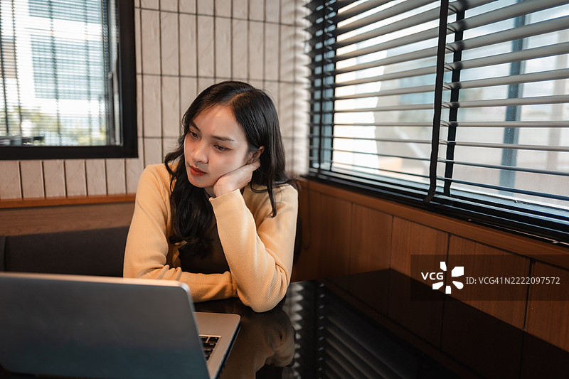 年轻的亚洲女性在热闹的咖啡馆里专心致志地使用笔记本电脑，展现出专注和高效的工作状态，周围氛围充满活力。图片素材