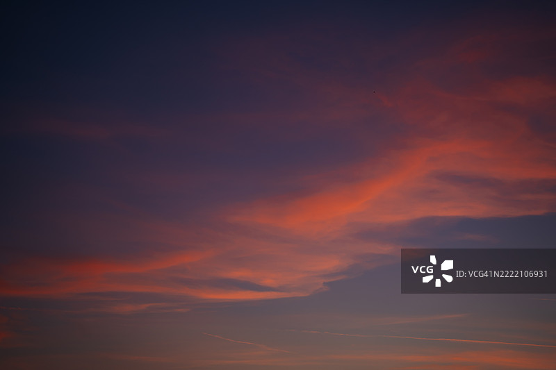 戏剧性的云彩在日落日出时的天空中，背景呈现出橙色、蓝色、紫色和粉色的梦幻低调效果。图片素材