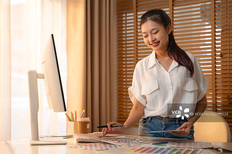 年轻的亚洲女性平面设计师在记录标志设计的笔记。色彩样本。艺术家在办公室的图形平板上绘制作品。平面设计师的创意编辑理念概念。图片素材