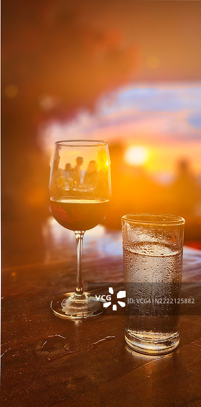 餐桌布置，配有酒杯、水杯，背景是柔焦的用餐者和海滩日落图片素材