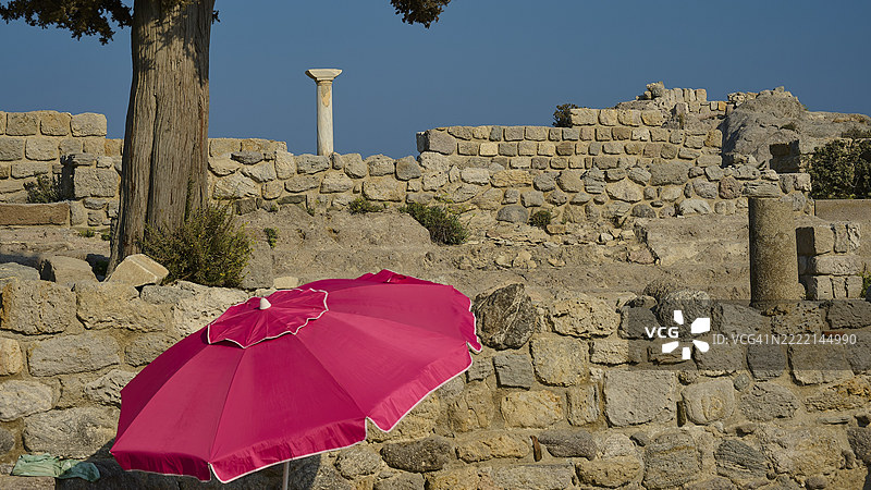 古老的遗址前景中有一把红色阳伞,背景是晴朗的蓝天,阿吉奥斯·斯特法诺斯海滩,阿吉奥斯·斯特法诺斯大教堂,阿吉奥斯·尼古拉斯小教堂,卡斯特里岛,科斯岛,多德卡尼斯群岛,希腊,欧洲图片素材