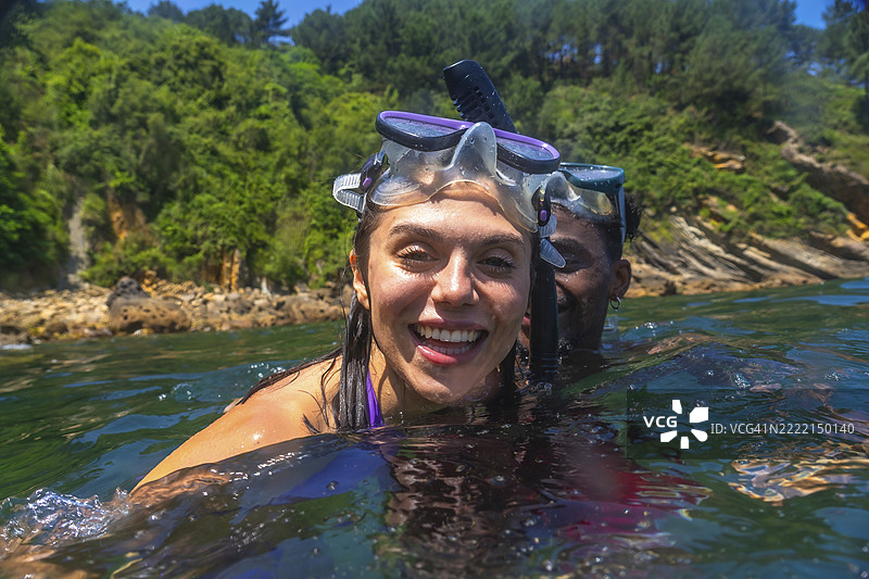 跨种族情侣在海中一起浮潜，周围环绕着充满活力的绿色海岸线，享受愉快的夏日冒险图片素材