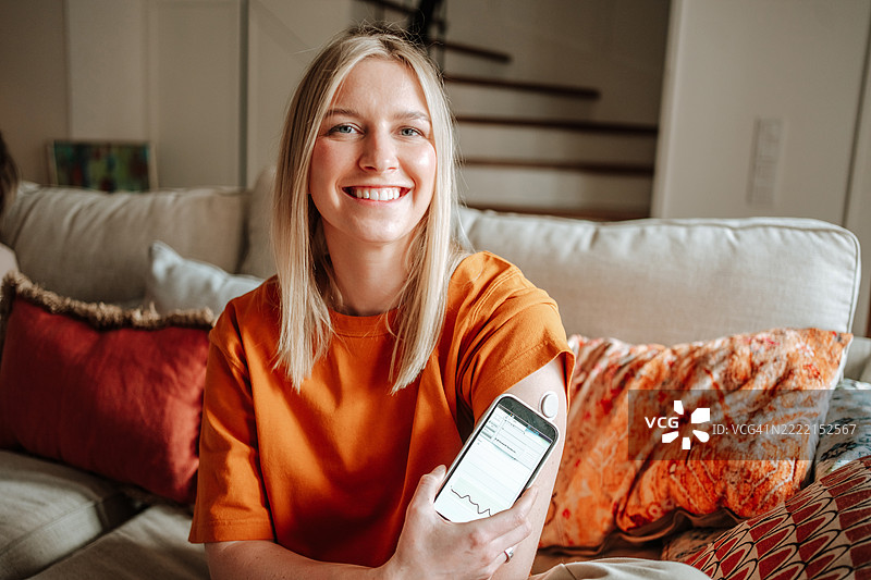 微笑的女性通过连接的应用程序和手臂传感器检查血糖图片素材