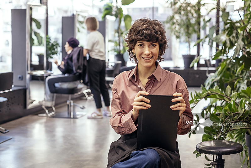 年轻女性美容院老板在现代植物装饰的工作室中自信微笑图片素材