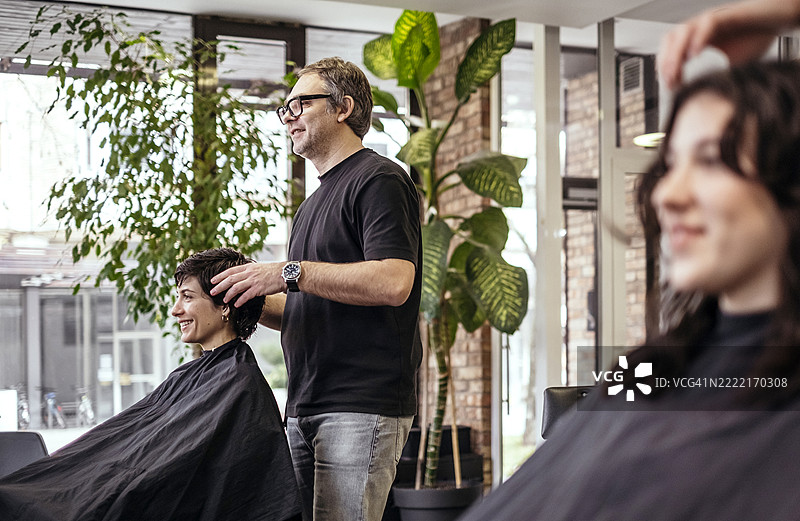 专业发型师在明亮现代的沙龙内为女性客户造型图片素材