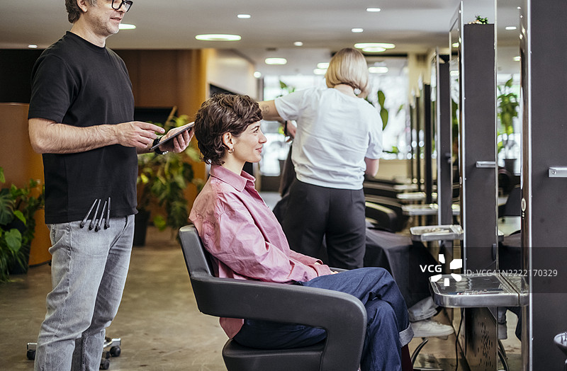 专业发型师在现代美容院为年轻女性剪发，光线自然。图片素材