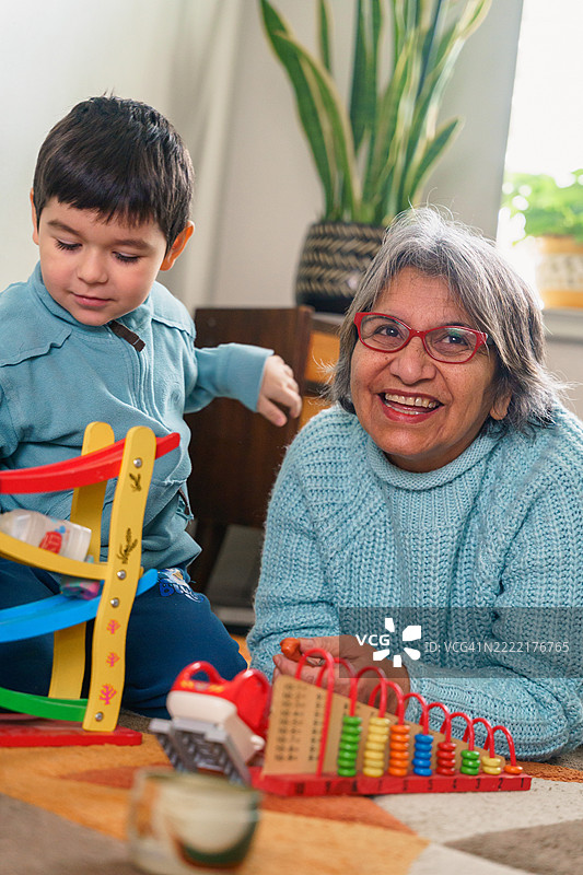 拉丁裔祖母和孙子在地板上玩玩具和算盘图片素材