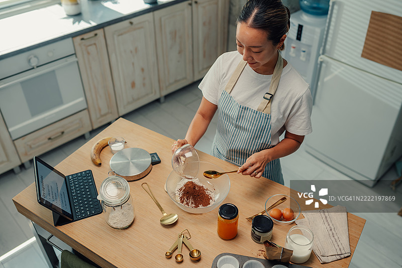 女人在平板电脑上跟着食谱，往混合物中加入可可粉图片素材