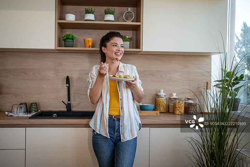年轻女性在现代厨房里吃新鲜沙拉图片素材