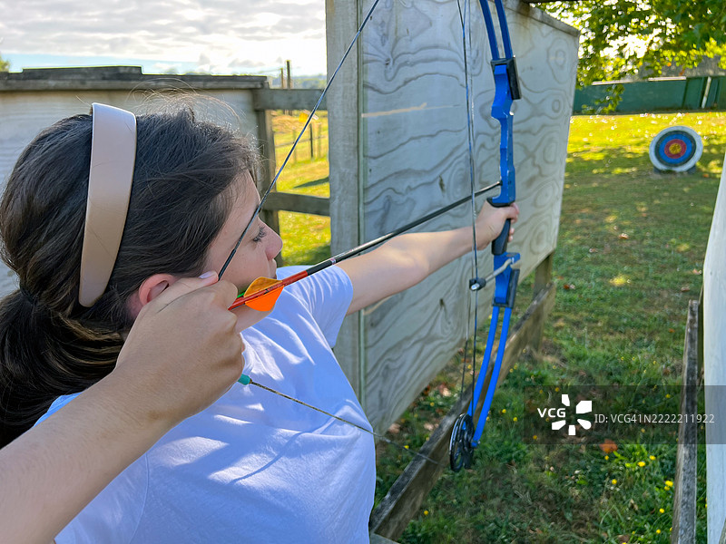 青少年女孩在旧农场的后院用弓箭射击靶子图片素材