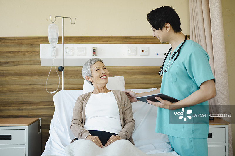 年轻医生微笑着向她的成熟患者解释诊断，患者手持平板，身处光线明亮的医院房间，营造出支持和关怀的氛围图片素材