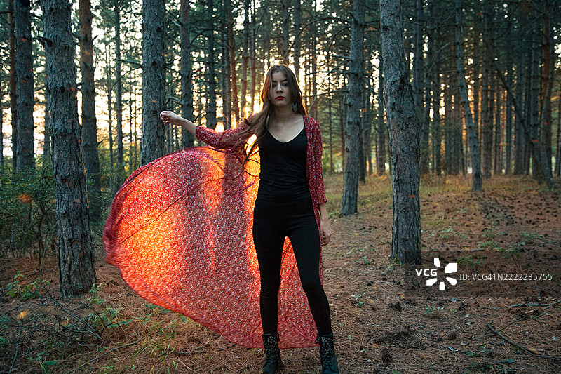 年轻女性穿着飘逸的裙子在森林中享受日落图片素材