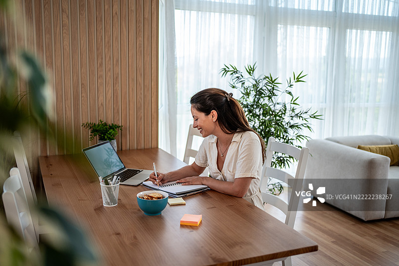年轻女性在家工作，正在笔记本上做笔记图片素材