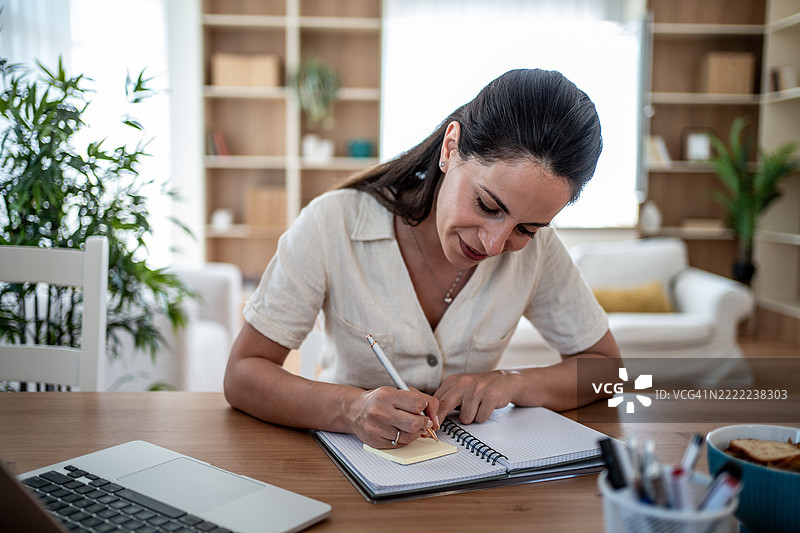 专注的女性在家办公桌上写笔记图片素材