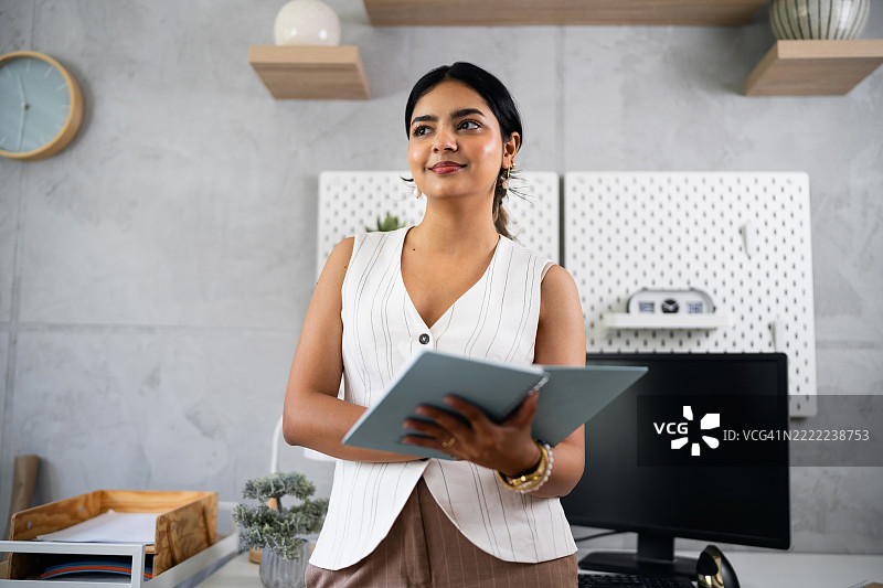 自信的女商人在现代办公室环境中手持文件夹站立图片素材