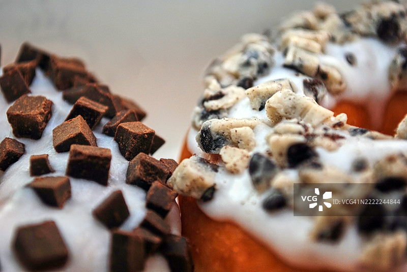 特写镜头展示了两个甜甜圈，一个上面撒满了浓郁的巧克力块，另一个则慷慨地覆盖着碎奥利奥饼干。图片素材