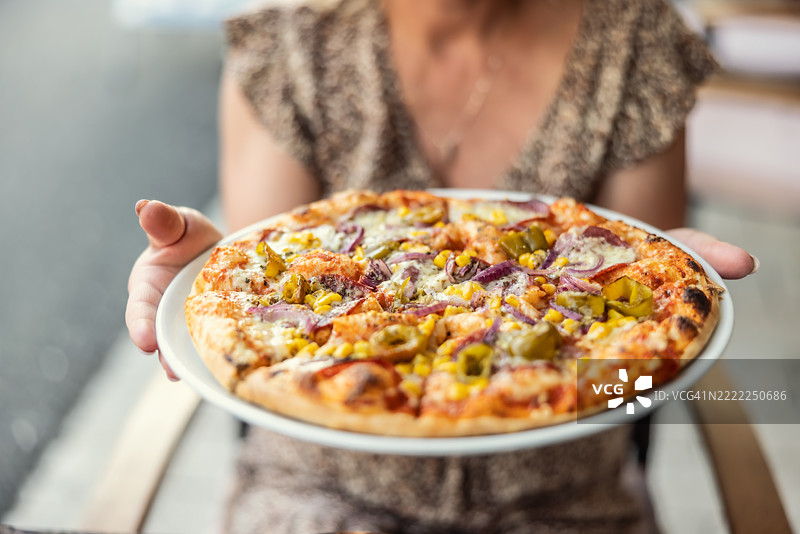 一位饥饿的女性正端着一盘新鲜的比萨饼。图片素材