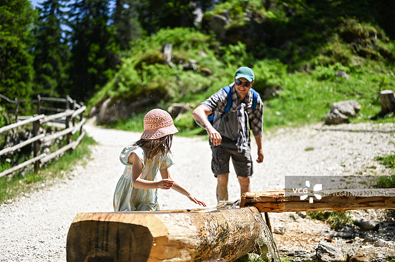 小女孩在木头上玩水，和父亲一起徒步旅行图片素材