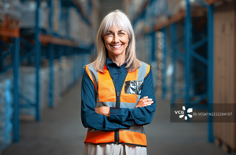 自信的女性高级员工穿着安全背心，站在现代化仓库中图片素材