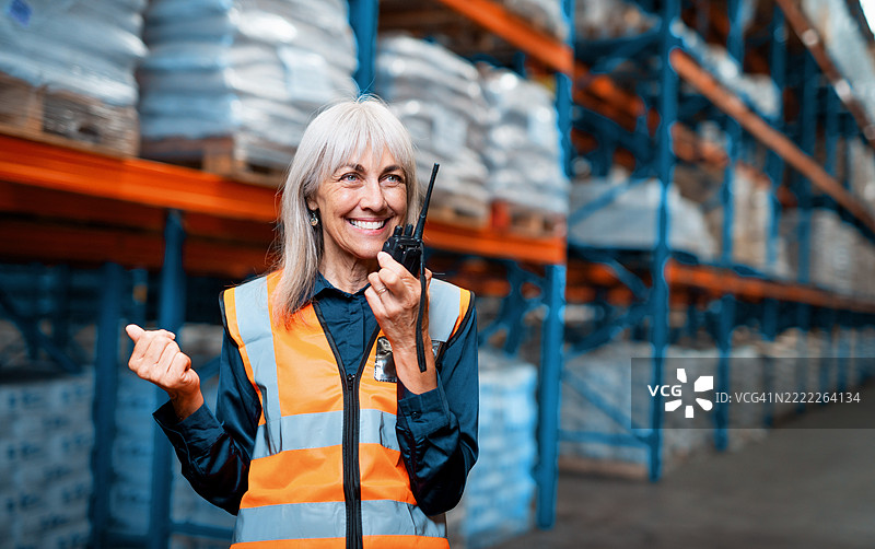 微笑的女性仓库工人穿着安全背心，在物流环境中通过对讲机进行沟通图片素材