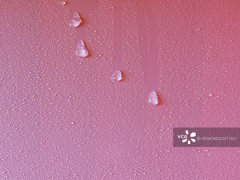 湿润的表面上有透明的水滴在粉色背景上滑动。图片素材