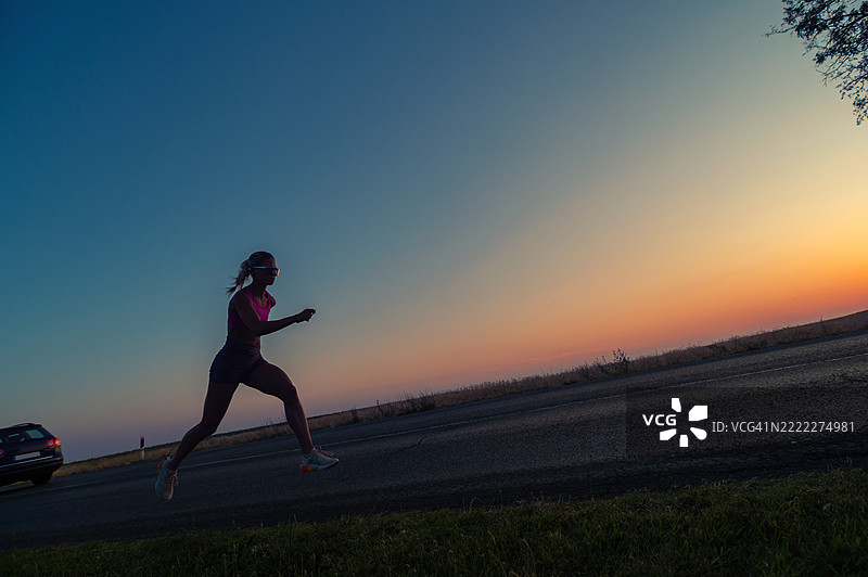 年轻的运动女性在夏季日落时在路上奔跑图片素材