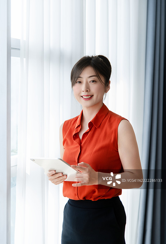 微笑的女商人在办公室窗前使用数字平板电脑图片素材
