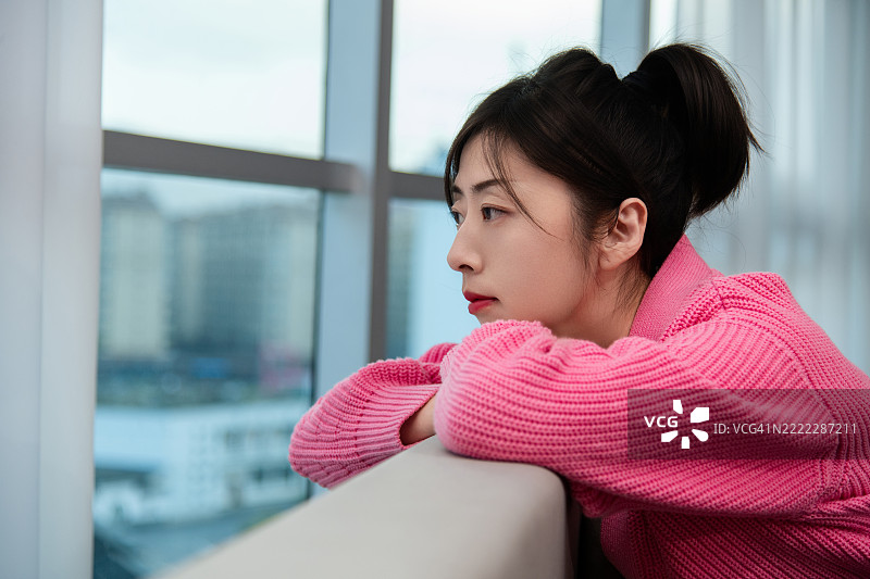 女人靠在沙发上，望着窗外。图片素材