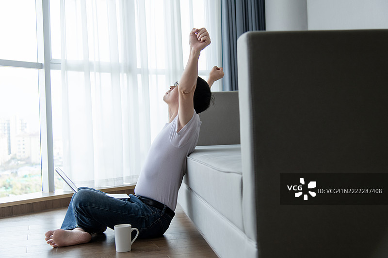 男子坐着用笔记本电脑并伸展身体图片素材