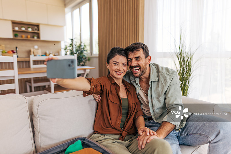 快乐的情侣在沙发上自拍，准备出发去度假图片素材