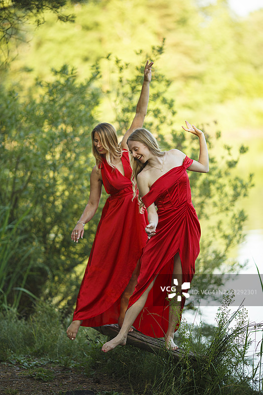 母女穿着红色连衣裙在大自然中优雅地在木头上跳舞图片素材
