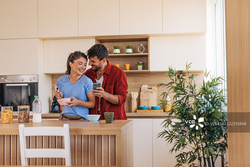 快乐的情侣在现代厨房享用早餐并使用社交媒体图片素材