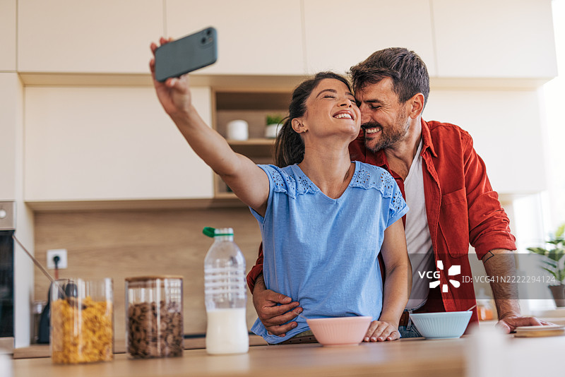 快乐的情侣在厨房吃早餐时自拍图片素材