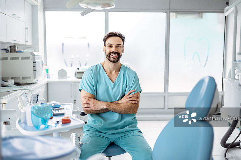友好的牙医自豪地站在牙科办公室里图片素材