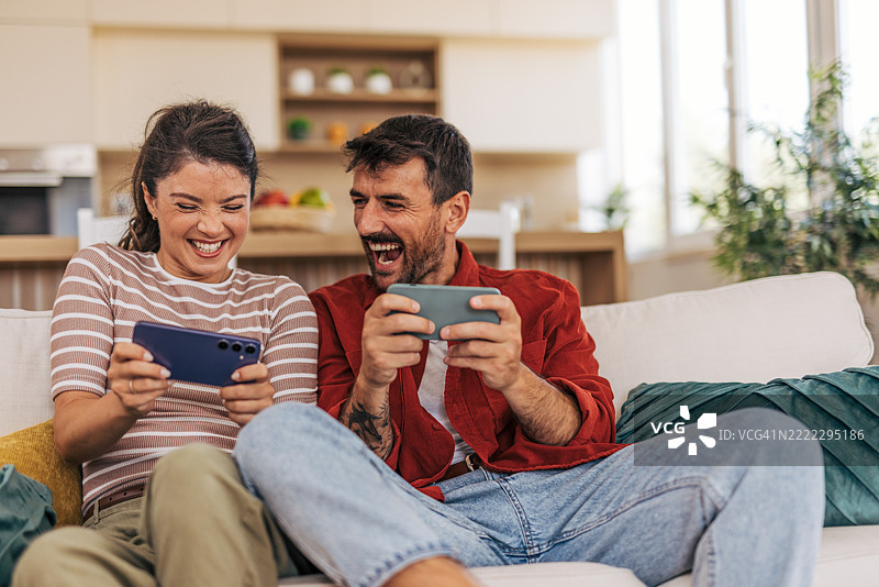 情侣在家沙发上放松，一起玩手机游戏图片素材