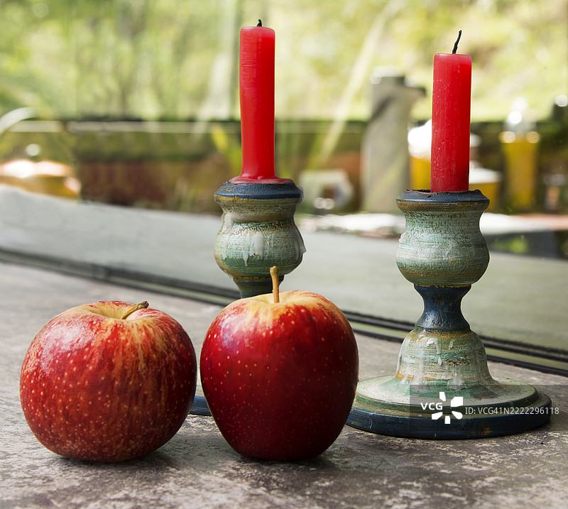 两个红苹果放在两个红色蜡烛台前。静物画。富含维生素，有助于降低胆固醇。图片素材