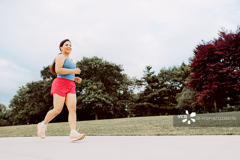 一位穿着运动服的女性在公园里慢跑，四周环绕着郁郁葱葱的绿树。图片素材