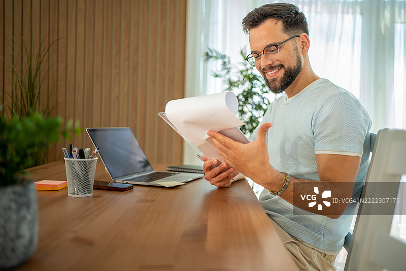微笑的自由职业者在家办公桌前阅读文件图片素材