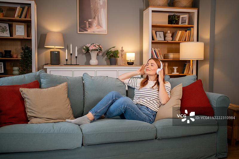 女人在舒适的客厅里戴着耳机放松地听音乐，坐在沙发上图片素材