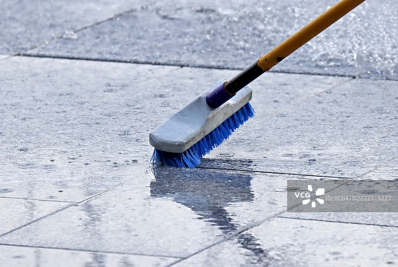 在潮湿的灰色瓷砖上用长柄刷手动清洁地面图片素材