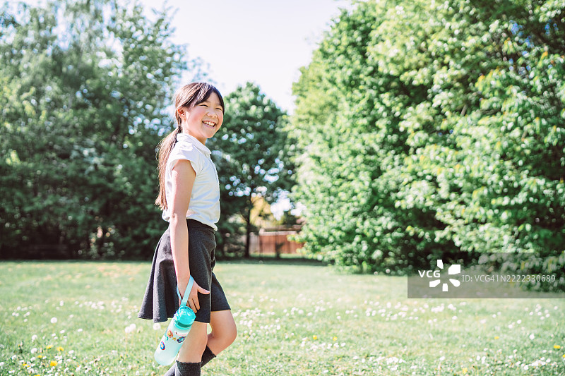 快乐的女学生在阳光明媚的日子里走在户外，手里拿着水瓶图片素材