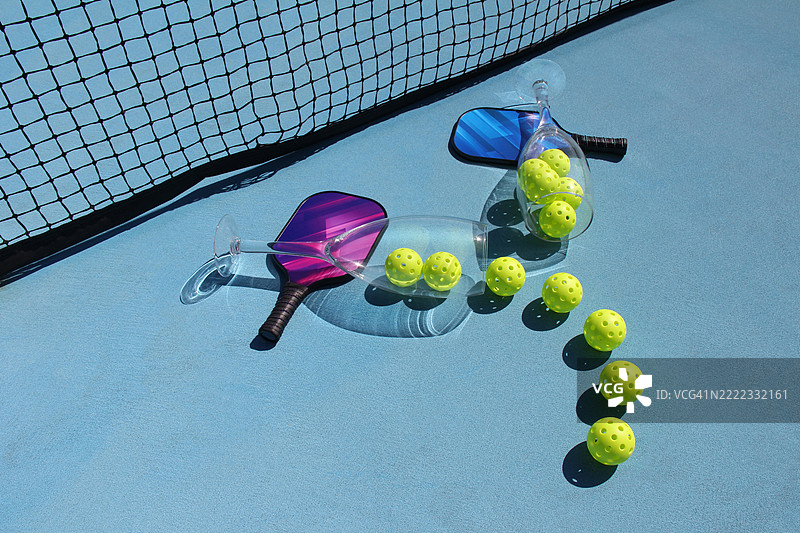 超大酒杯与蓝色场地上的泡菜球、球拍和网在户外摆放图片素材